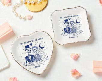 May include: Two white ceramic ring dishes with gold trim, featuring a blue skeleton couple design and the text "Till Death Do Us Part." One dish is heart-shaped, the other square. Each has a wedding date.
