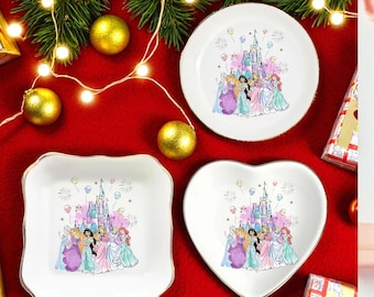 May include: Set of three white ceramic dishes in round, square, and heart shapes. Each dish features a colorful illustration of princesses in front of a castle. Gold trim edges the dishes, set against a red background with Christmas decorations.