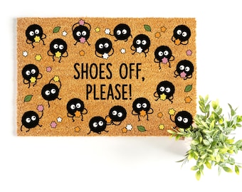 May include: A rectangular tan coir doormat featuring the black text SHOES OFF, PLEASE! in the center. The mat is decorated with multiple small, round, black fuzzy creatures with large white eyes, interspersed with tiny colorful stars and green leaves.