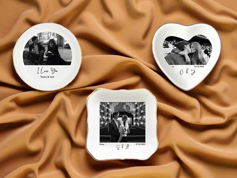 May include: Three white ceramic dishes with gold trim, each featuring a black and white photograph. One is round with "I Love You" text, another heart-shaped, and the third square. The dishes are on a gold fabric.