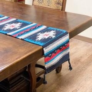 Peut inclure: Un chemin de table bleu et noir avec un motif géométrique et des glands frangés. Le chemin de table est en tissu tissé et a un design sud-ouest.