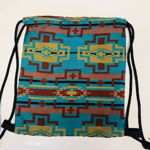 Op de afbeelding: Een blauwe, bruine en gele gepatroneerde trekkoordtas met zwarte trekkoorden. De tas heeft een geometrisch ontwerp.