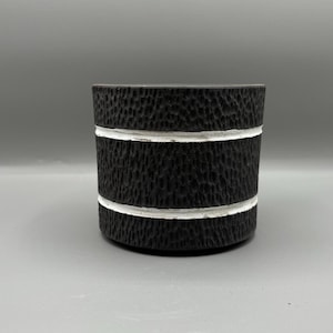 May include: A black ceramic planter with a textured surface and two white bands around the rim.