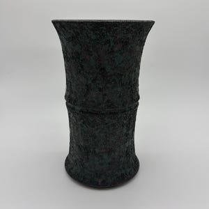 May include: A dark green textured vase with a flared top and base. The vase has a cylindrical shape with a textured surface. The vase is approximately 10 inches tall.