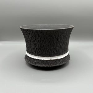 May include: A black ceramic planter with a textured surface and a white band around the rim.