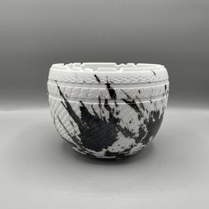 May include: A white ceramic bowl with a black and white splatter design. The bowl has a textured surface and a slightly raised rim.