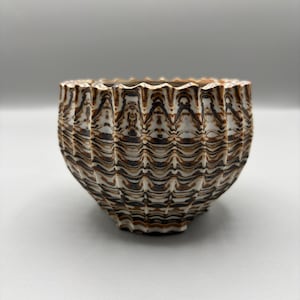 May include: A ceramic bowl with a textured, ridged exterior. The bowl features a pattern of brown and black marbling against a white background. The rim has a scalloped edge. The bowl is a decorative item.