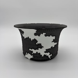 May include: A black and white ceramic planter with a unique design. The exterior features a textured, dark pattern against a white background. The planter has a flared rim and a cylindrical shape, suitable for indoor or outdoor use.