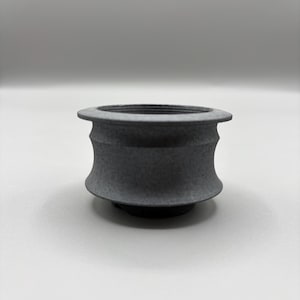 May include: A dark gray, cylindrical object with a flared top and base. The object has a textured surface and a concave midsection. The design is symmetrical, and the object appears to be made of a solid material.