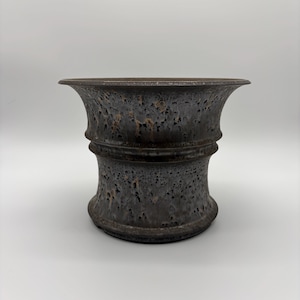 May include: A ceramic planter with a flared rim and a cinched middle section. The surface features a dark, mottled glaze with deep charcoal, black, and subtle bronze-toned speckles, creating a textured, volcanic appearance across the entire exterior.