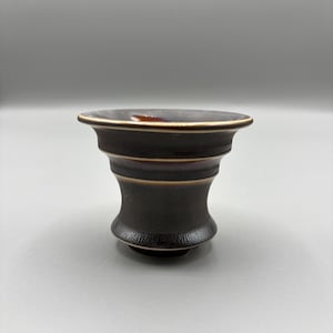 May include: A dark brown ceramic bowl with a wide rim and a textured base. The bowl has a layered design with a lighter brown accent near the top. The bowl is likely for serving or display.