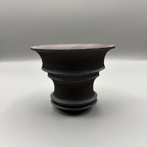 May include: A dark, textured ceramic bowl with a wide, flared rim and a detailed, tiered base. The interior of the bowl has a reddish-brown hue, contrasting with the black exterior. The bowl's design suggests a handcrafted aesthetic.