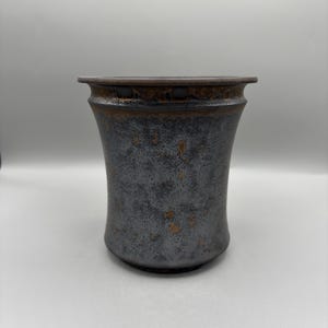 May include: A ceramic vessel with a flared rim and a tapered body. The surface features a dark, mottled glaze in shades of charcoal gray and black, accented with subtle, scattered flecks of metallic copper and bronze throughout the exterior.