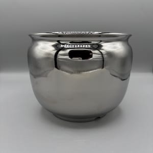 May include: A shiny, silver-colored bowl with a rounded shape and a wide opening. The bowl has a smooth, reflective surface, creating a mirror-like effect. The design is simple and modern, suitable for various uses.