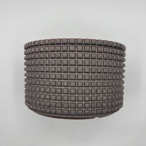 May include: A cylindrical planter with a dark brown finish and a repeating grid pattern of raised square studs covering the entire exterior surface. The vessel features a flat rim and a consistent, textured geometric design throughout its body.