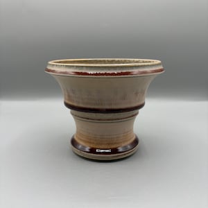May include: A ceramic vase with a wide, flared top and a bulbous base. The vase is primarily beige with brown accents around the rim, midsection, and base. The design has a rustic, handcrafted appearance, suitable for home decor.