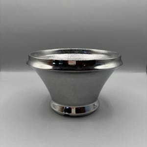 May include: A silver-colored, decorative bowl with a flared, conical shape. The bowl has a wide, flat rim and a rounded base. The surface is smooth and reflective, with a polished finish. The bowl is designed to be a decorative item.