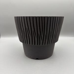 May include: A dark gray, textured plant pot with a unique, ridged design around the top. The pot has a slightly flared shape and a solid base, suitable for indoor or outdoor use. The ridged pattern adds a modern touch to this decorative planter.