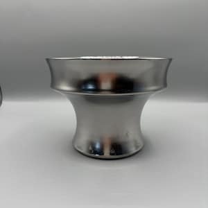 Könnte beinhalten: Eine silberfarbene, dekorative Schale mit ausgestelltem Boden und breitem, geschwungenem Rand. Die Schale hat eine glatte, metallische Oberfläche und ein symmetrisches Design. Die Schale ist wahrscheinlich aus Metall und für dekorative Zwecke geeignet.