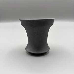 May include: A dark gray, textured ceramic vase with a unique hourglass shape. The vase has a wide base and a flared top, with a textured surface. The vase is approximately 4 inches tall.