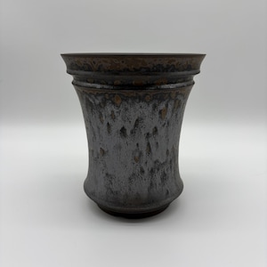 May include: A ceramic vase with a flared rim and a tapered body. The exterior features a mottled glaze with a dark brown base color, transitioning into a textured, metallic silver-grey finish with visible brown speckles throughout the surface.