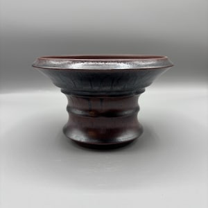 May include: A handcrafted ceramic vessel with a wide, flared rim and a dark, earthy color palette. The exterior transitions from a deep brown to a black hue, with a textured surface. The base has a rounded, tiered design. This decorative piece is suitable for home decor.