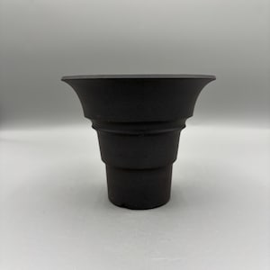 May include: A matte black vessel with a tiered, stepped silhouette. The object features a narrow cylindrical base that widens into a series of three distinct, stacked circular sections, culminating in a wide, flared, and flat-edged rim.