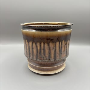 Può includere: Un vaso da fiori in ceramica marrone e bianco con un design testurizzato. Il vaso ha una base larga e rotonda e un bordo leggermente svasato.