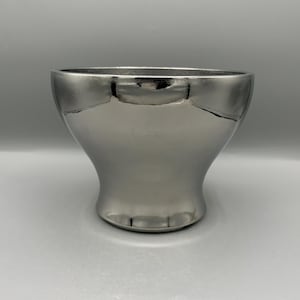 May include: A silver-colored bowl with a wide, rounded top and a flared base. The bowl has a smooth, reflective surface, and the interior is not visible. The bowl is likely made of metal or a metallic-finished material.