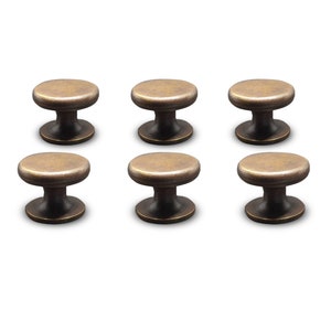 Könnte beinhalten: Sechs antike Messing-Schrankknöpfe mit pilzförmigem Design. Jeder Knopf hat eine abgerundete Oberseite und einen dunkelbronzenen Sockel, was eine Vintage-Ästhetik erzeugt. Ideal, um Möbeln einen Hauch von klassischem Stil zu verleihen.
