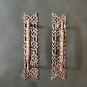 Puede incluir: Dos tiradores de puerta de bronce antiguo con un diseño de nudo celta. Los tiradores son de metal y tienen un acabado texturizado.