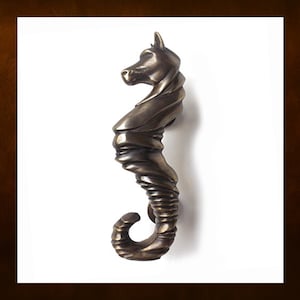 Puede incluir: Un llamador de puerta de bronce en forma de caballito de mar. El caballito de mar está intrincadamente detallado con un acabado texturizado y su cola está enroscada alrededor de su cuerpo.