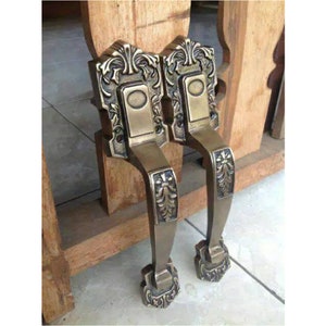 Puede incluir: Dos manillas de puerta de latón adornadas con intrincados diseños florales. Las manillas están fijadas a un marco de puerta de madera.