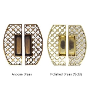 Pode incluir: Duas puxadores de porta decorativas em latão. Um par é em latão antigo, o outro em latão dourado polido. Cada puxador tem formato oval com design de treliça e uma alça retangular. Medidas em cm.