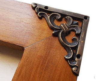 May include: A wooden picture frame with ornate brass corner accents. The frame has a warm brown finish and the corner accents have a detailed floral design.