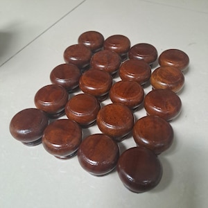 May include: A collection of eighteen round, dark brown wooden knobs arranged in a grid pattern. Each knob features a smooth, polished surface with visible wood grain patterns and a rounded, mushroom-like shape with a slightly tapered base.