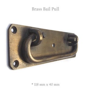 May include: Brass bail pull handle with a rectangular base and a curved handle. The handle measures 118 mm by 40 mm.