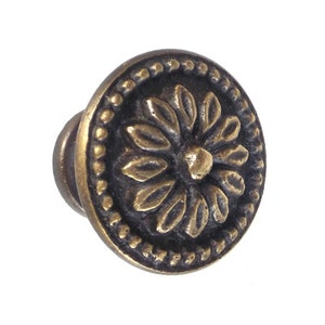 May include: A round, brass cabinet knob with a decorative floral design. The knob has a dark brown finish and a raised, textured center.