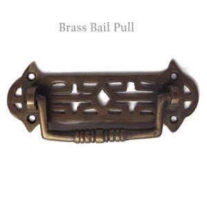 May include: Brass bail pull with an intricate, geometric design. The pull has a rectangular shape with a curved handle.