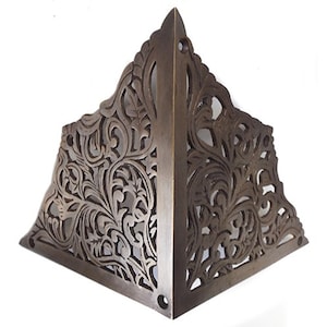 May include: A decorative brass corner bracket with an intricate floral design. The bracket is made of solid brass and has a dark, antique finish.