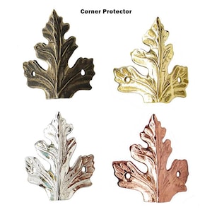 May include: Four decorative corner protectors in leaf shapes. The protectors are in bronze, gold, silver, and copper finishes. Each leaf has a detailed vein pattern and two holes for mounting. The text "Corner Protector" is at the top.
