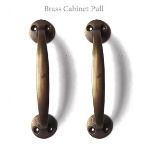 May include: Two brass cabinet pulls with a curved design. The pulls have a smooth, polished finish.
