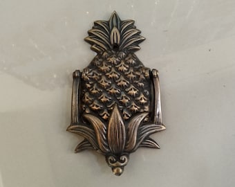 Könnte beinhalten: Ein Türklopfer aus Messing in Form einer Ananas mit einem detaillierten Design. Der Türklopfer hat die Form einer Ananas mit einem Blattwerk und einem Ring zum Klopfen.