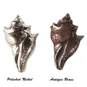 May include: Two seashell-shaped cabinet knobs. One is polished nickel, the other is antique brass. The polished nickel knob is shiny and silver. The antique brass knob is a darker, bronze colour. The text "Polished Nickel" and "Antique Brass" are below each knob.