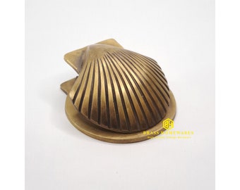 May include: A brass door knocker shaped like a scallop shell. The knocker has a detailed, textured design and is mounted on a round base.