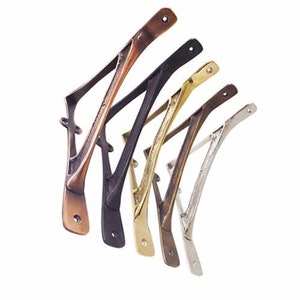 Könnte beinhalten: Fünf Metall-Regalböcke in verschiedenen Ausführungen: Kupfer, Schwarz, Gold, Silber und Nickel. Die Böcke sind in Form eines stilisierten Buchstabens 'V' mit einer geschwungenen Oberseite geformt.