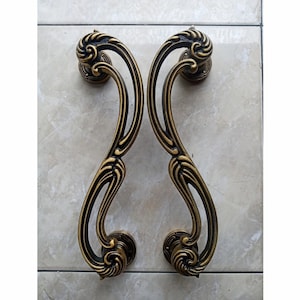 May include: A pair of ornate gold door handles with a decorative, swirling design. The handles are made of metal and have a polished finish.