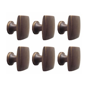 May include: Six antique brass square cabinet knobs with a slightly rounded edge. The knobs have a simple, elegant design.