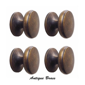 May include: Four antique brass cabinet knobs. Each knob has a rounded, disc-shaped face and a cylindrical base. The knobs are a warm, aged brass color, with visible texture. The text "Antique Brass" is at the bottom.