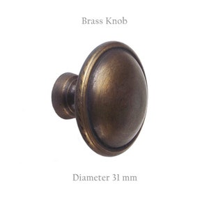 May include: A brass knob with a rounded, slightly domed face and a stem. The knob has a dark, aged finish with a diameter of 1.2 inches. The text "Brass Knob" is above the knob, and "Diameter 31 mm" is below it.